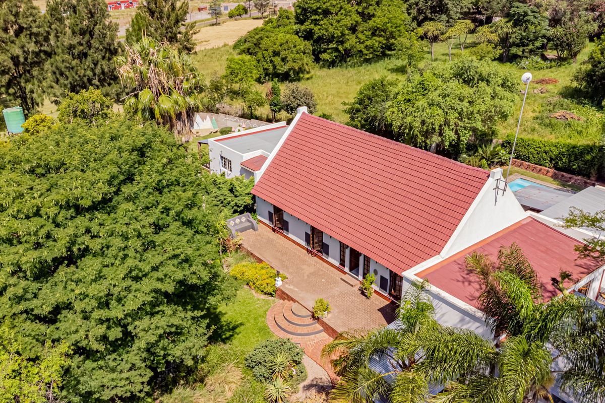 Aerial view of a small holding property featuring a main dwelling with a tiled roof, expansive brick patio, swimming pool, and established garden surroundings.