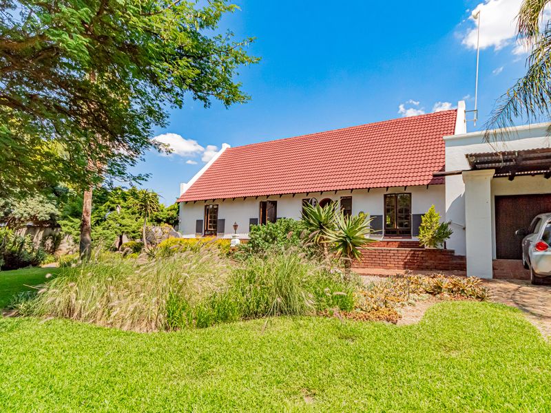 Front elevation of a well-maintained small holding featuring a classic tiled roof, established garden, and a paved driveway with a covered carport.