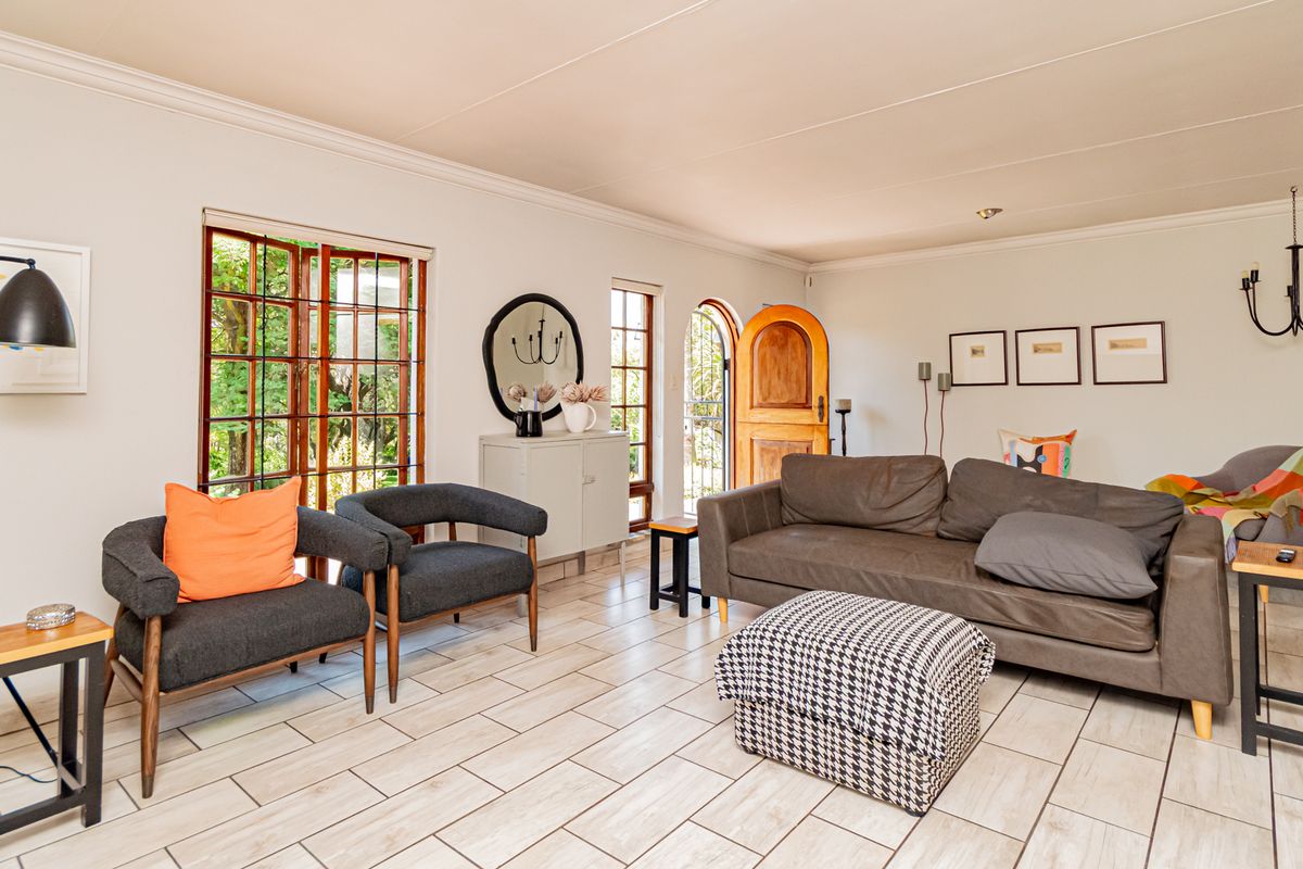 A bright and spacious living room featuring tiled flooring, coved ceilings, and natural light flowing through wooden framed sliding doors and an arched entrance.