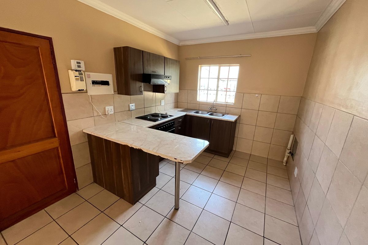 A functional kitchen featuring built-in cabinetry, a breakfast bar, electric hob, and double bowl sink with tiled splashbacks and flooring.