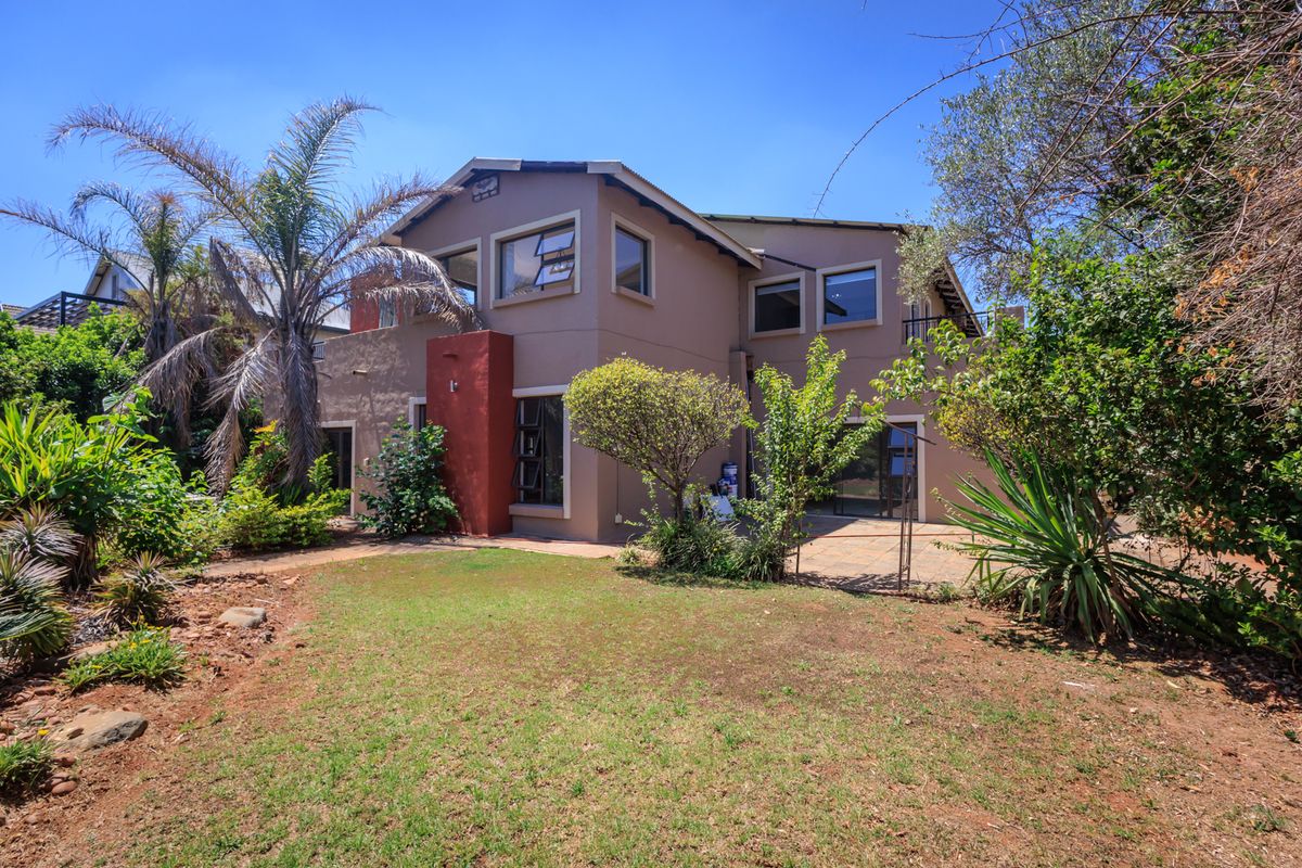 Rear view of a two-story residential property featuring a paved patio area, established garden, and large windows.