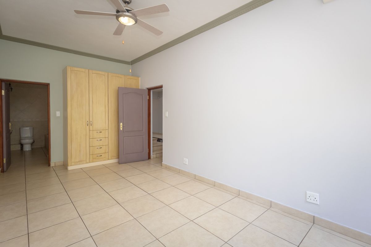 An empty bedroom featuring tiled flooring, built-in wooden cupboards, a ceiling fan, and direct access to an en-suite bathroom.