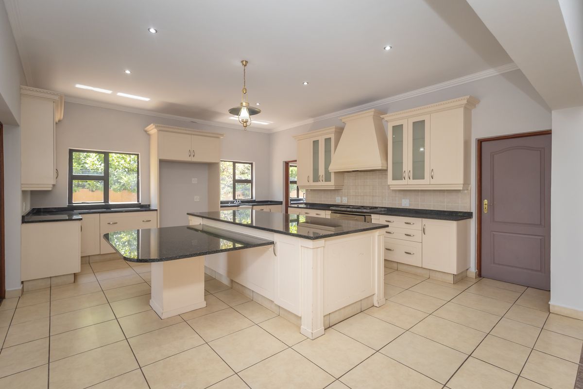Spacious kitchen featuring cream cabinetry, granite countertops, a large central island, and tiled flooring, offering a clean and functional layout.