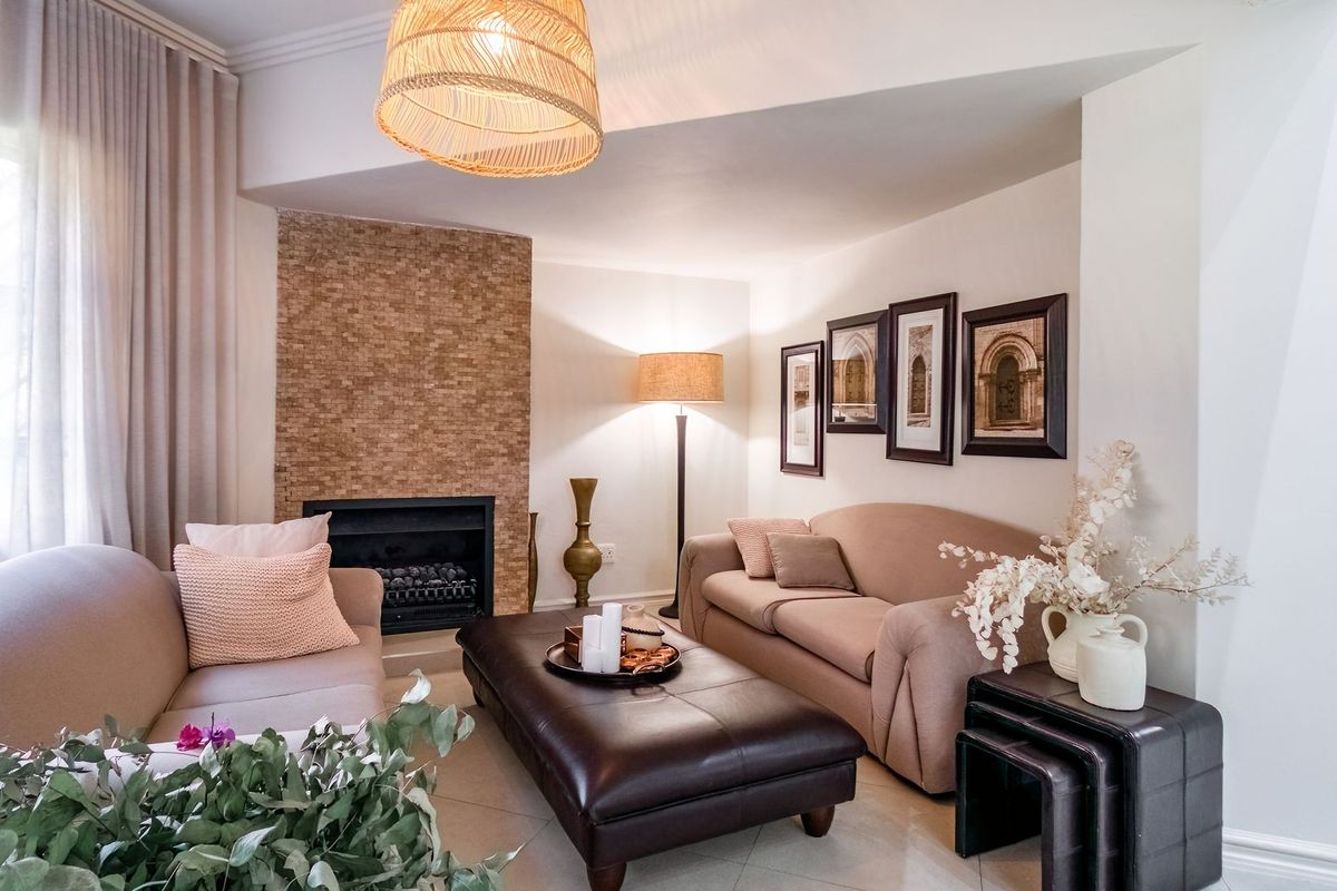 A comfortable living room featuring a built-in fireplace with a textured stone surround, tiled flooring, and large windows with elegant curtains.
