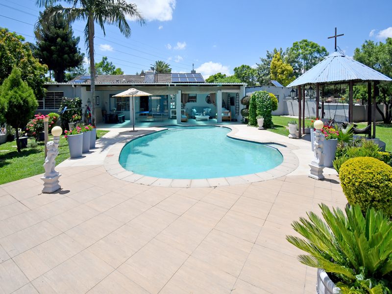 A spacious backyard featuring a swimming pool, paved patio area, and a gazebo, set within a well-maintained garden.