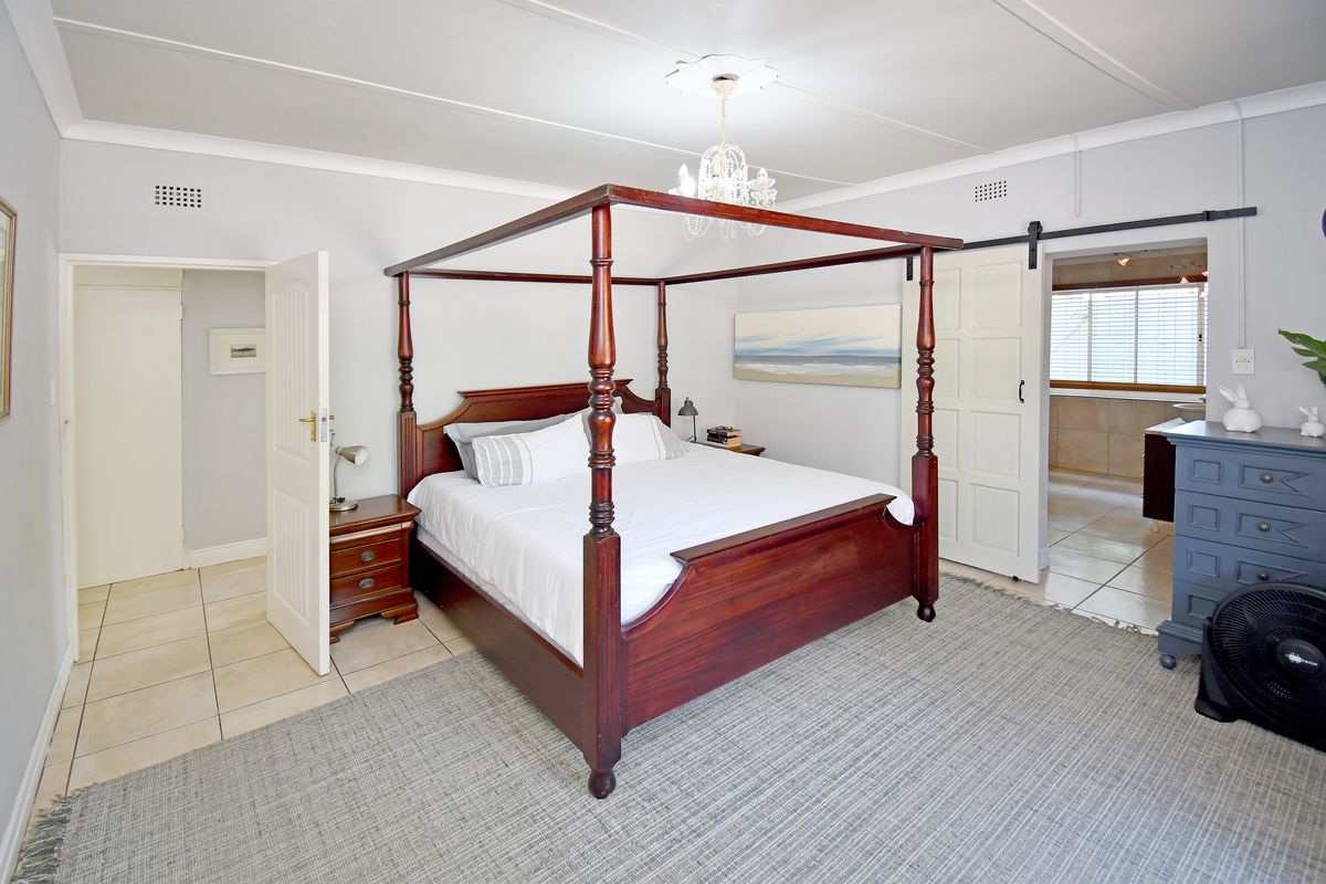 Spacious bedroom featuring tiled flooring, a ceiling rose with chandelier, and a sliding barn door leading to an adjoining bathroom.