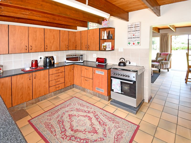 A functional kitchen featuring wood-finish cabinetry, granite countertops, a freestanding stove, and exposed timber ceiling beams, with direct access to an adjacent living area.