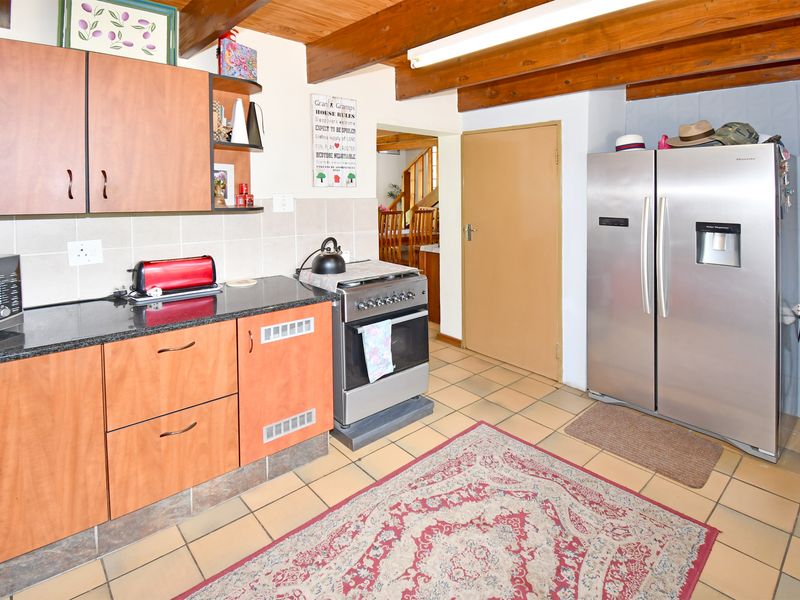 A functional kitchen featuring laminate cabinetry, granite countertops, tiled flooring, and exposed timber ceiling beams, offering a traditional aesthetic with practical layout.