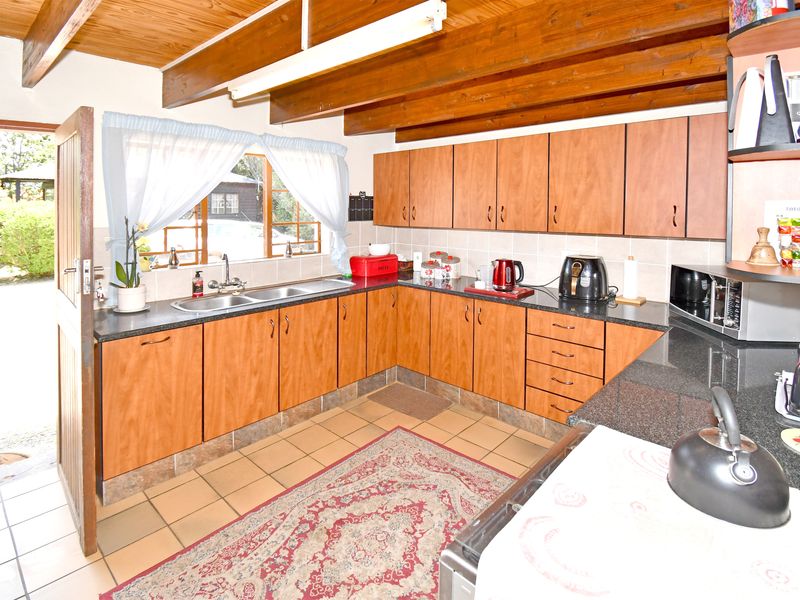 A functional kitchen featuring laminate cabinetry, granite countertops, double basin sink, and exposed timber ceiling beams with direct access to the garden.