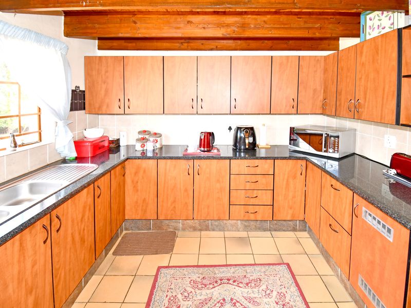 A functional U-shaped kitchen featuring wood-look cabinetry, granite countertops, double sink, and exposed timber ceiling beams.