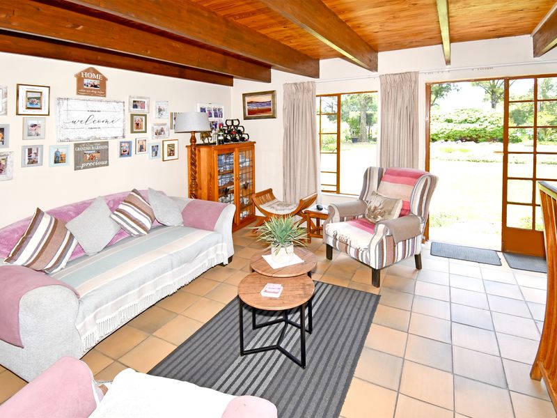 A living room featuring exposed timber ceiling beams, tiled flooring, and direct access to the garden through timber-framed glass sliding doors.