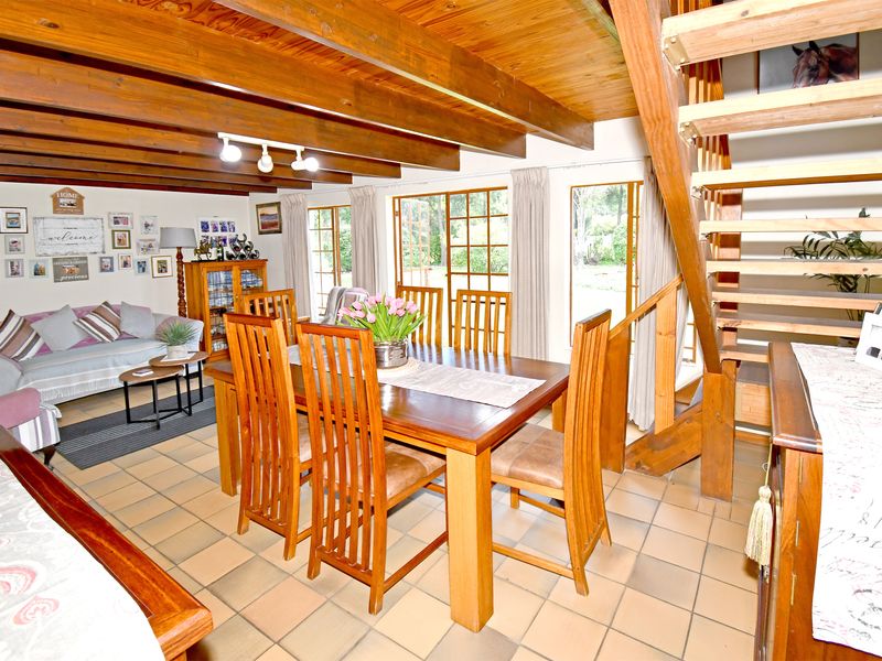 Open-plan living and dining area featuring exposed timber ceiling beams, tiled flooring, and a timber staircase leading to the upper level.