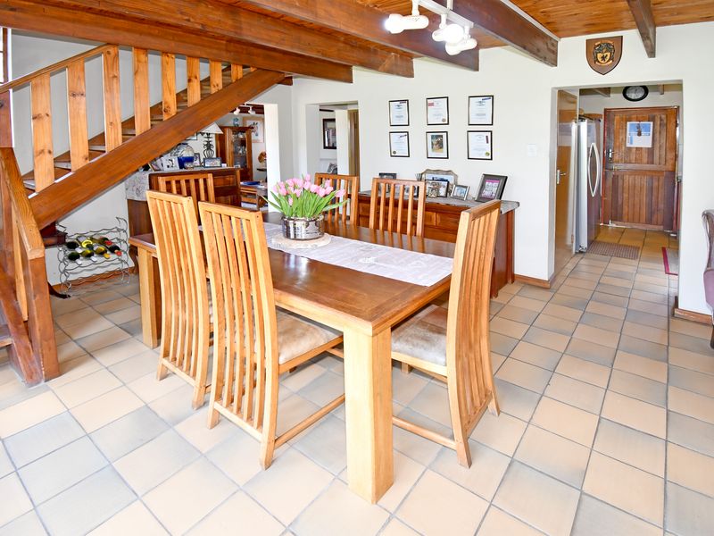 Dining area featuring exposed timber ceiling beams, a wooden staircase, and neutral ceramic floor tiles, providing a warm and rustic atmosphere.
