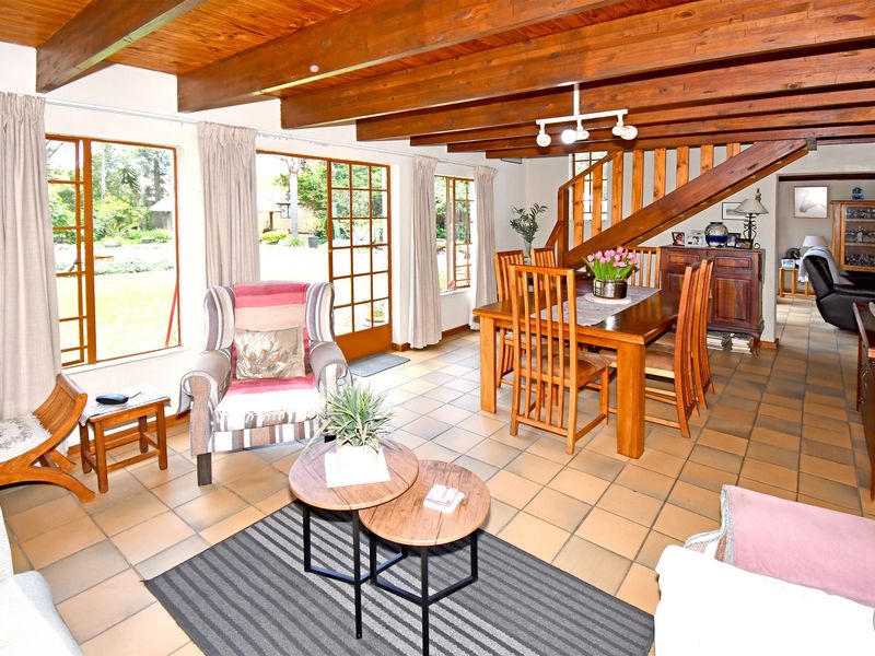 Spacious open-plan living and dining area featuring exposed timber ceiling beams, tiled flooring, and direct access to the garden through timber-framed glass doors.