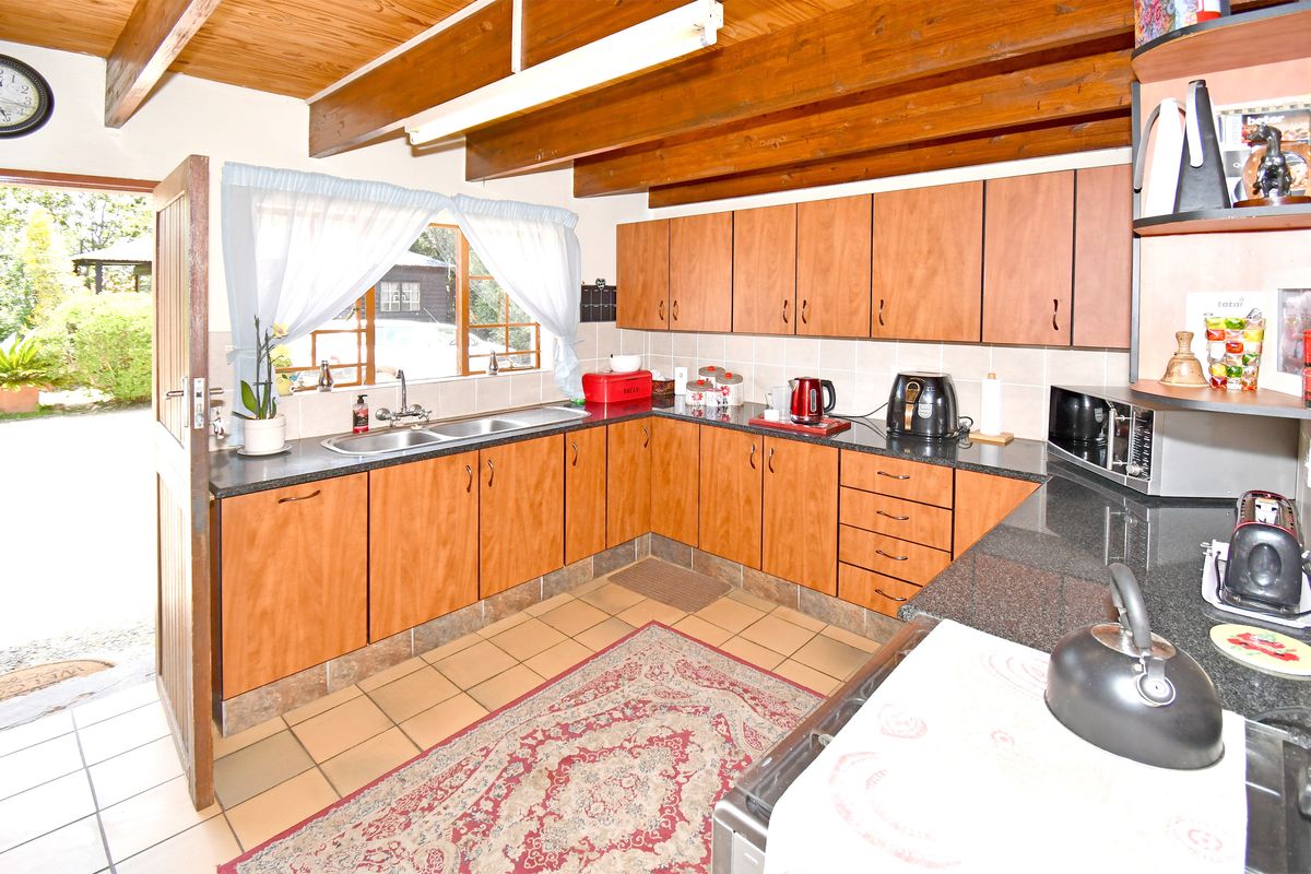 A functional kitchen featuring laminate cabinetry, granite countertops, double basin sink, and exposed timber ceiling beams with direct access to the garden.