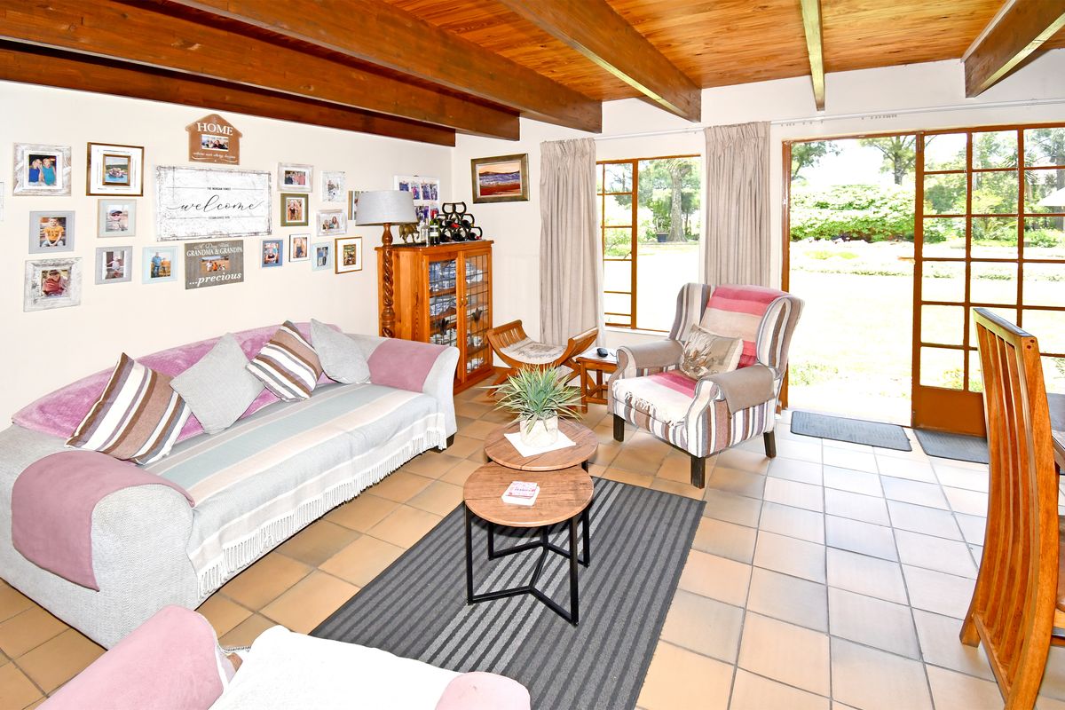 A living room featuring exposed timber ceiling beams, tiled flooring, and direct access to the garden through timber-framed glass sliding doors.