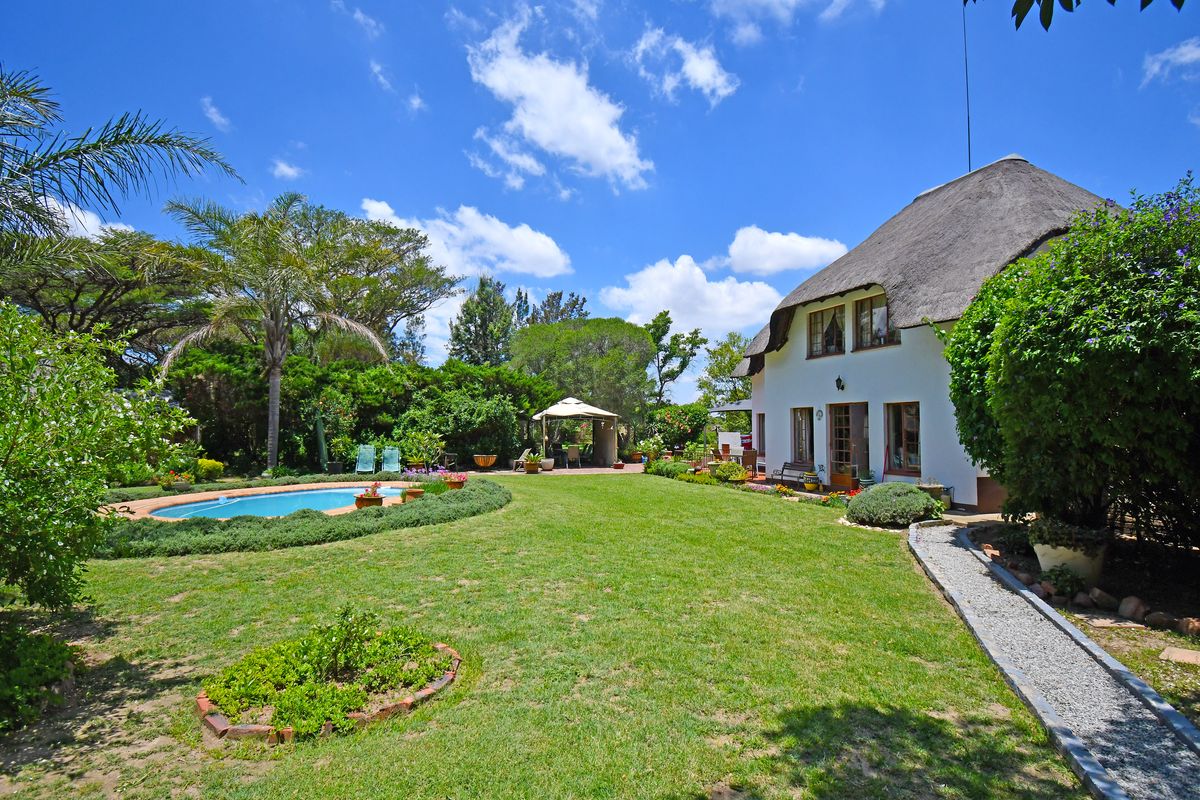 A spacious rear garden featuring a well-maintained lawn, a swimming pool, and a charming house with a traditional thatched roof.