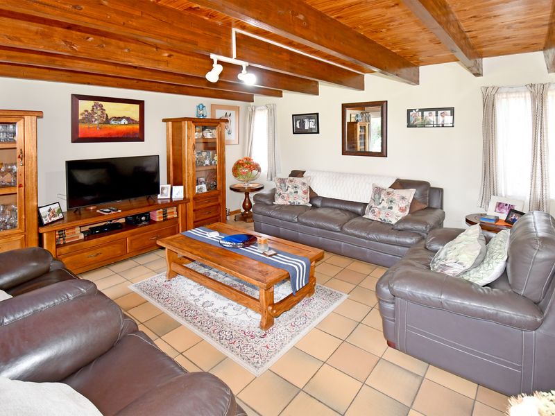 A comfortable living room featuring exposed timber ceiling beams, ceramic tile flooring, and functional track lighting, offering a warm and traditional aesthetic.