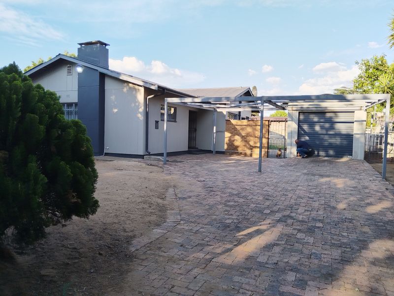 Front exterior view of the house featuring a paved driveway, a metal carport structure, and a single garage.