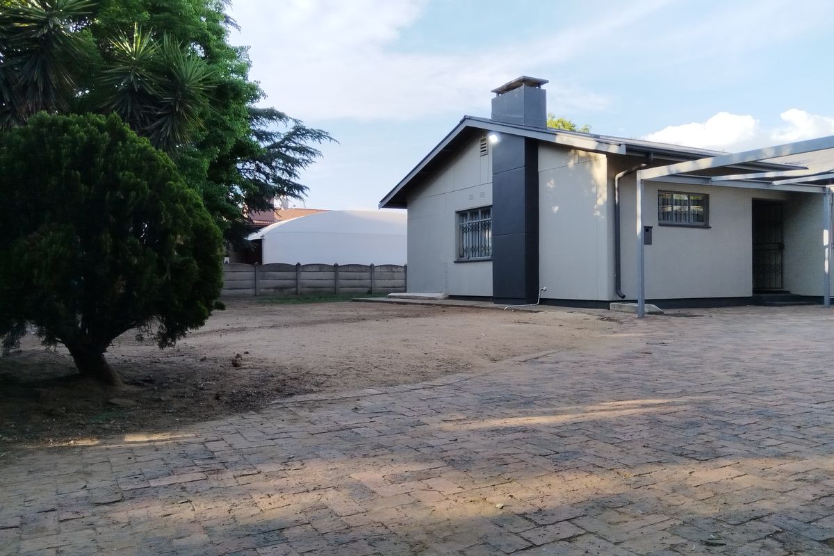 Rear view of the property featuring a paved driveway, a chimney, and a covered patio area with a surrounding precast concrete wall.