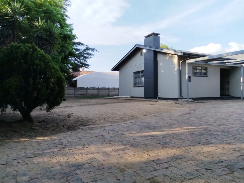 Rear view of the property featuring a paved driveway, a chimney, and a covered patio area with a surrounding precast concrete wall.