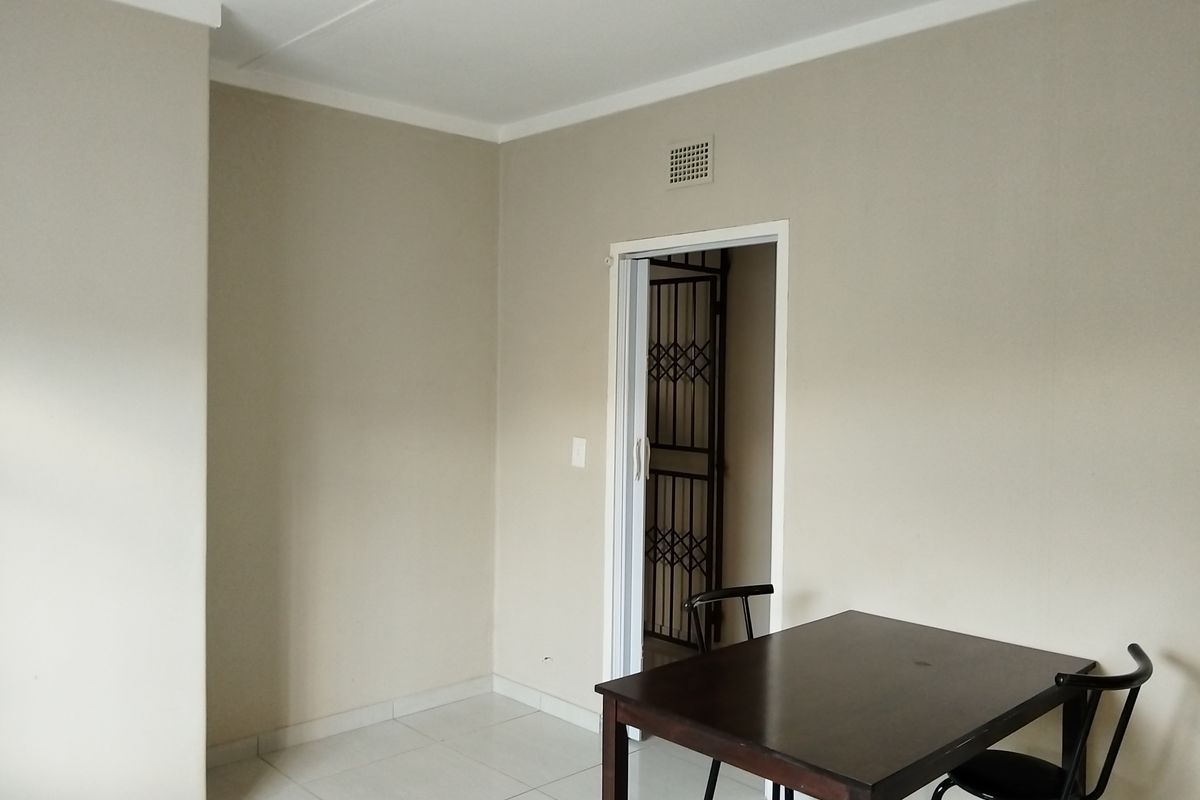 A neutral-toned living area featuring tiled flooring, coving, and a secure doorway leading to an adjacent space.
