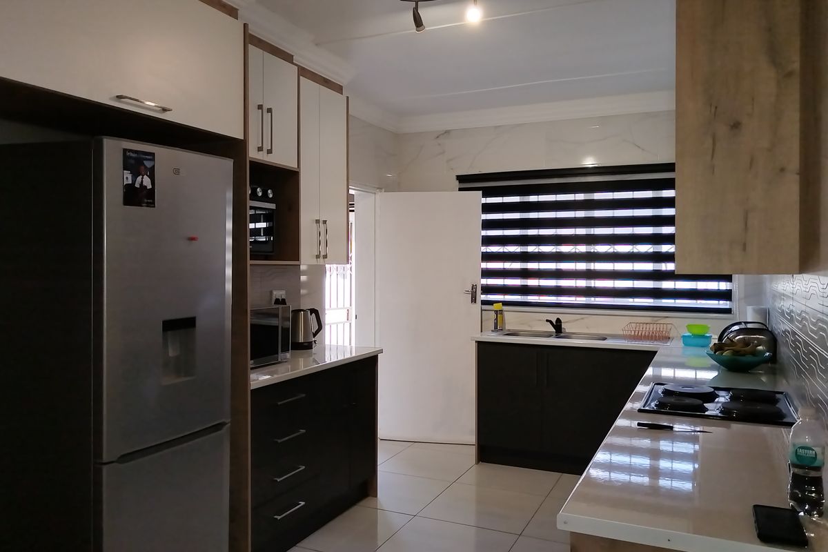 Modern kitchen featuring sleek two-tone cabinetry, stone countertops, integrated hob and oven, and tiled flooring with ample natural light.