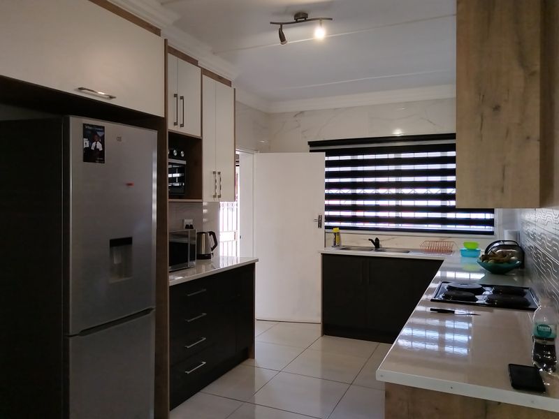 Modern kitchen featuring sleek two-tone cabinetry, stone countertops, integrated hob and oven, and tiled flooring with ample natural light.