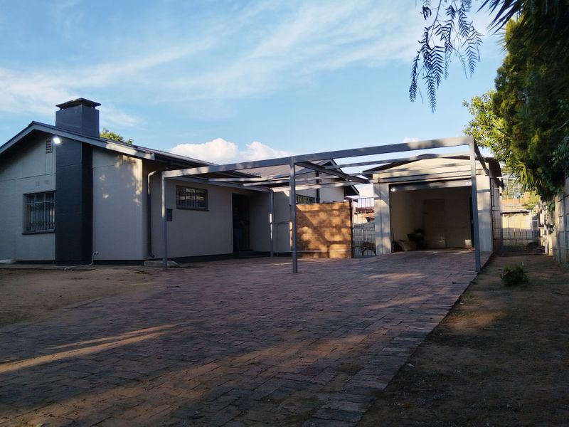 Front exterior view featuring a paved driveway, a modern metal carport structure, and an attached garage with a chimney.