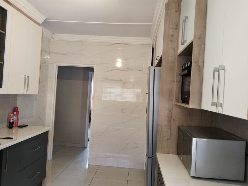 Modern kitchen featuring sleek two-tone cabinetry, marble-effect wall tiling, stone countertops, and integrated appliance housing with crown molding details.