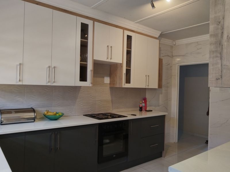 Modern kitchen featuring two-tone cabinetry, stone countertops, built-in oven, electric hob, and stylish tiled backsplash with neutral floor tiles.