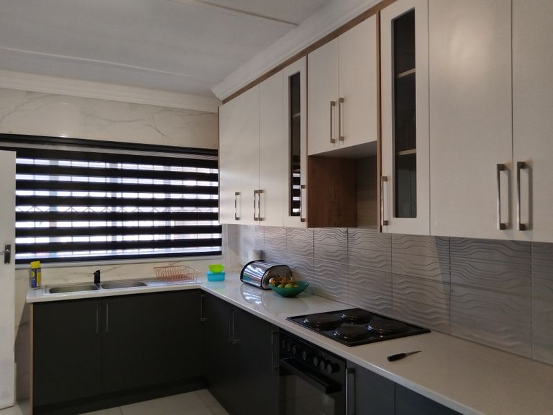 Modern kitchen featuring two-tone cabinetry, stone countertops, integrated electric hob and oven, and a tiled backsplash with a double basin sink.