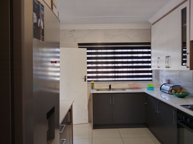 Modern kitchen featuring dark grey lower cabinetry, white upper cabinets, stone countertops, marble-look splashback tiles, and integrated appliances.