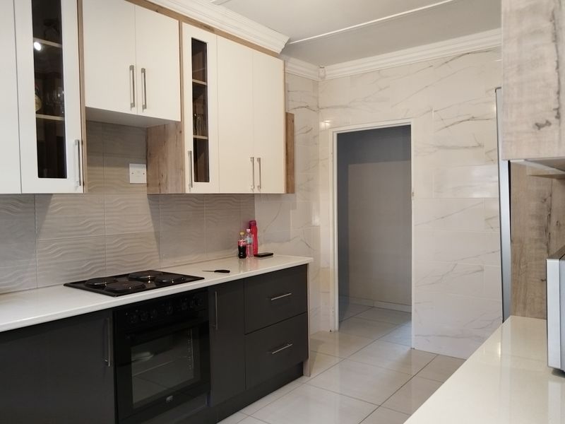 Modern kitchen featuring two-tone cabinetry, stone countertops, integrated electric hob and oven, and elegant marble-effect wall tiling.