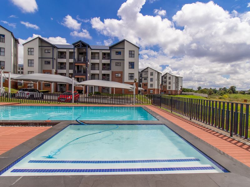 A well-maintained communal swimming pool and wading area featuring composite decking, metal fencing, and shade sails within an apartment complex.