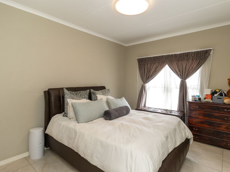 A well-lit bedroom featuring neutral wall tones, tiled flooring, and a window with installed curtain rails.