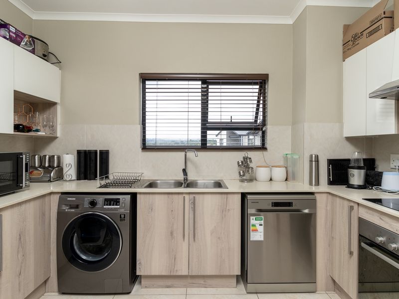 Modern kitchen featuring light wood-grain cabinetry, stone countertops, a double sink, built-in oven, extractor fan, and integrated space for laundry and dishwasher appliances.