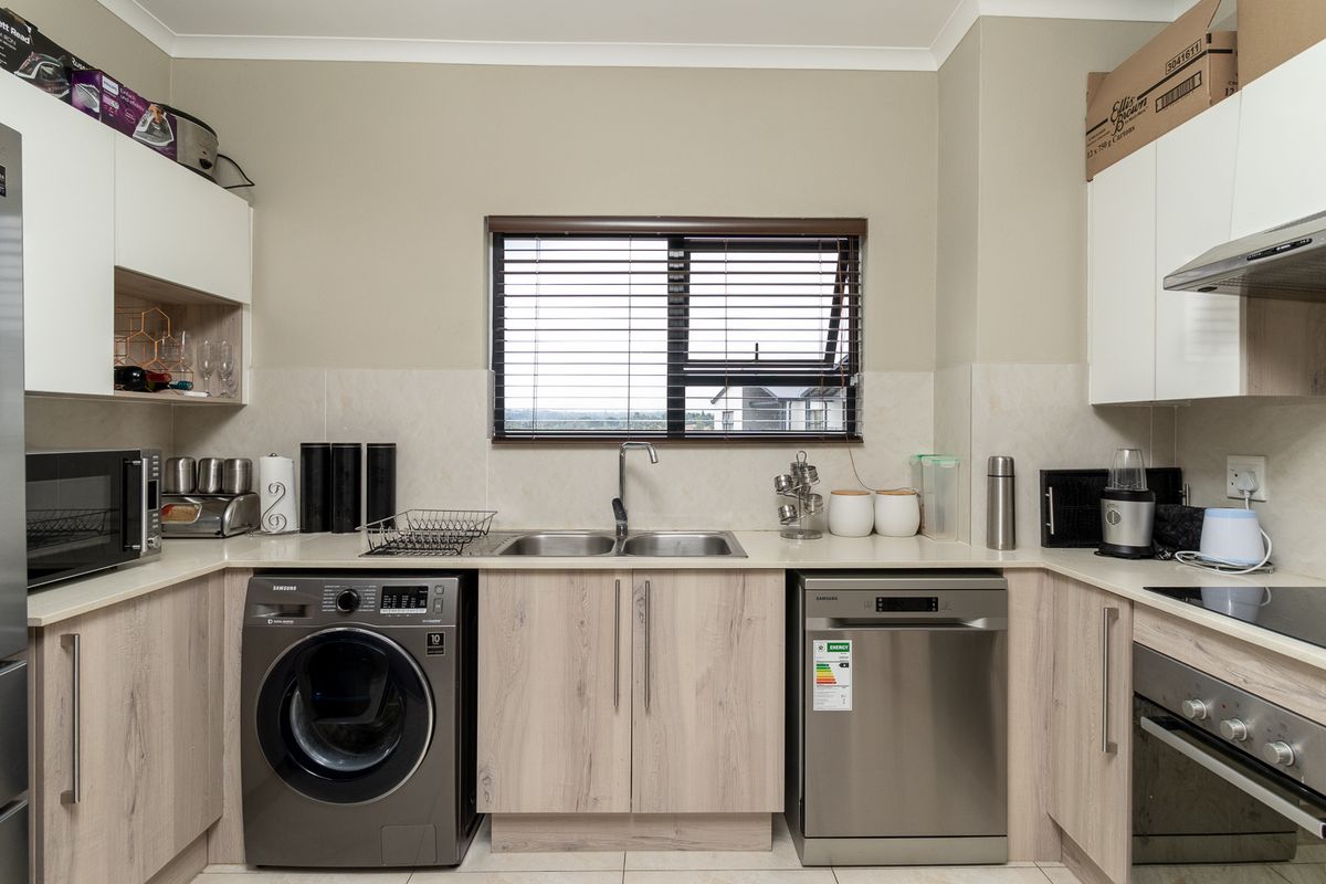 Modern kitchen featuring light wood-grain cabinetry, stone countertops, a double sink, built-in oven, extractor fan, and integrated space for laundry and dishwasher appliances.