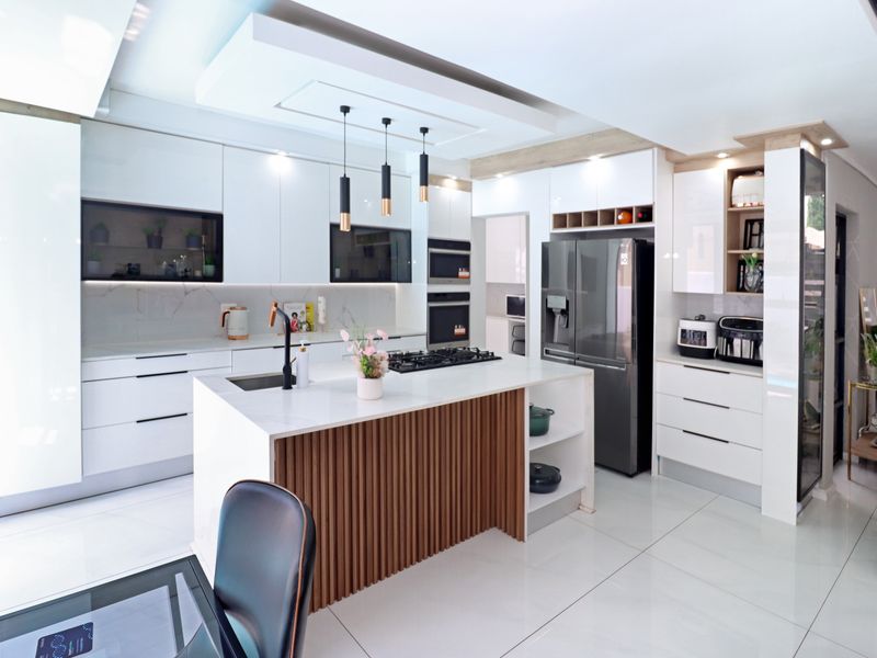 Modern, high-end kitchen featuring a central island with slatted wood detailing, stone countertops, integrated appliances, and sleek white cabinetry with recessed lighting.