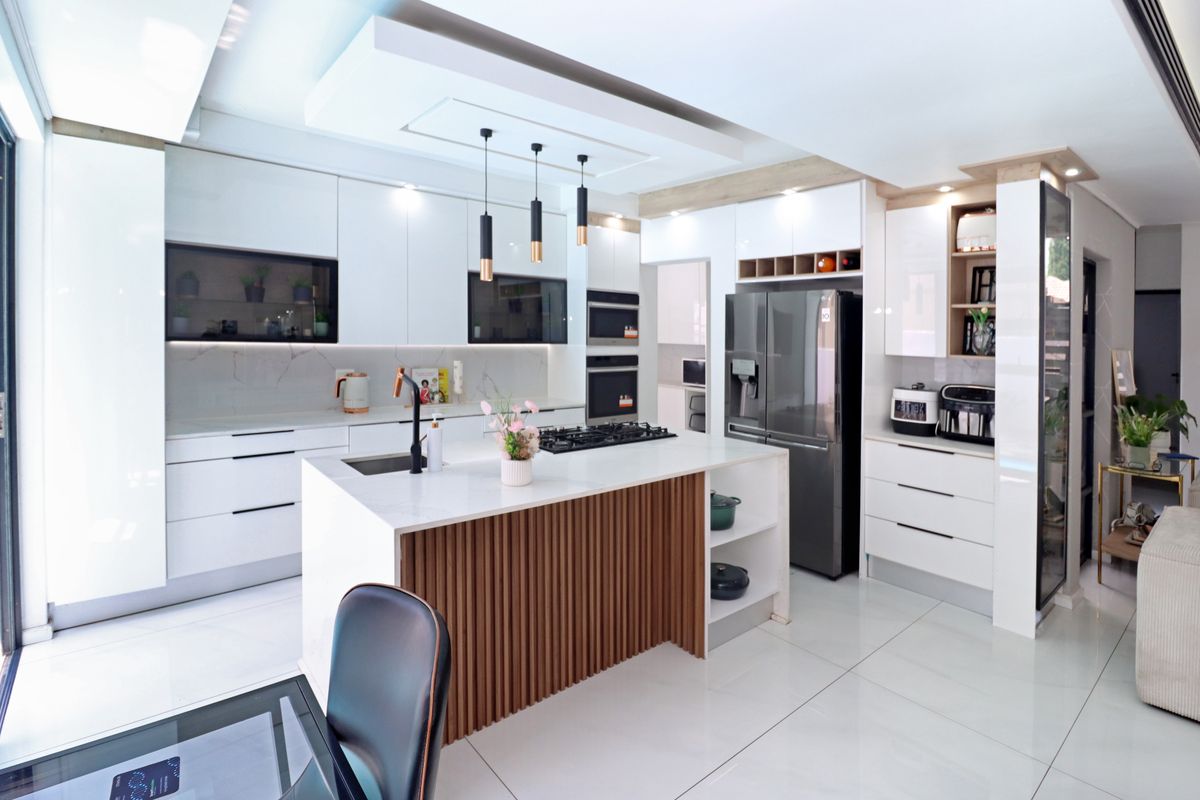 Modern, high-end kitchen featuring a central island with slatted wood detailing, stone countertops, integrated appliances, and sleek white cabinetry with recessed lighting.