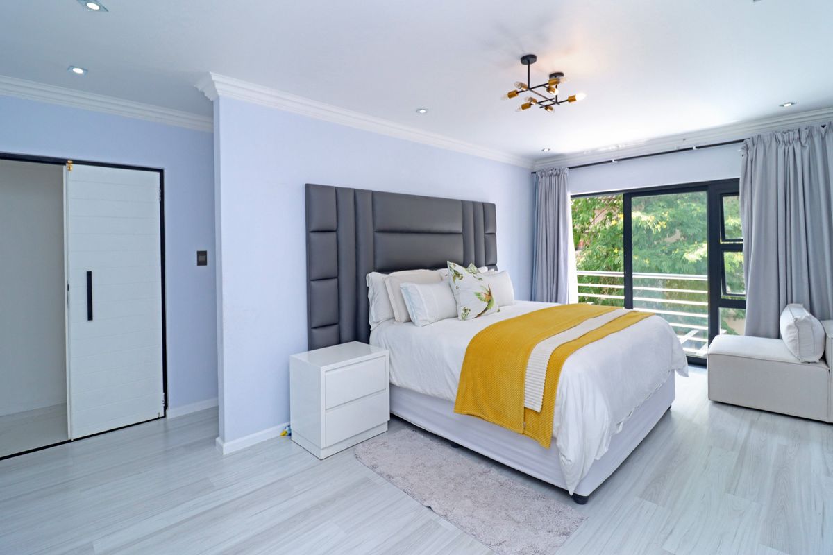 A bright and modern bedroom featuring light laminate flooring, crown molding, recessed lighting, and a large sliding glass door leading to an outdoor balcony.
