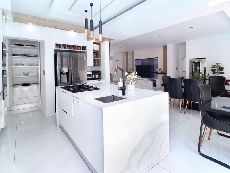 Modern open-plan kitchen featuring a large stone-topped island, gas cooktop, integrated cabinetry, and a spacious walk-in pantry, seamlessly flowing into the dining area.