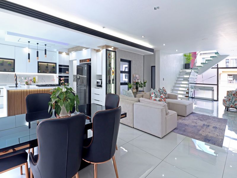 Modern open-plan living area featuring a sleek kitchen with island, high-gloss cabinetry, and a striking staircase with glass balustrade and polished floor tiles.