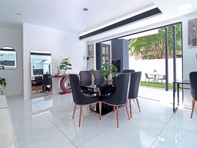 Modern dining area featuring large format floor tiles, recessed lighting, and seamless indoor-outdoor flow through stacking glass doors to the garden.
