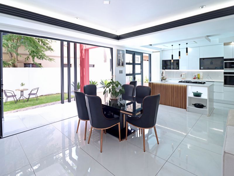Modern open-plan kitchen and dining area featuring high-gloss cabinetry, a central island with integrated appliances, and seamless access to the outdoor patio.
