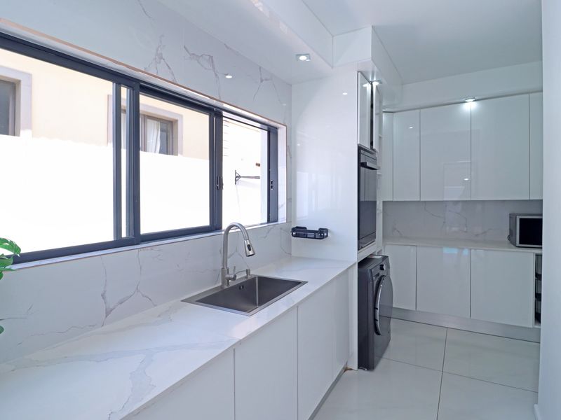 Modern, minimalist kitchen featuring high-gloss white cabinetry, marble-look quartz countertops, integrated appliances, and sleek tiled flooring in a bright, clean space.