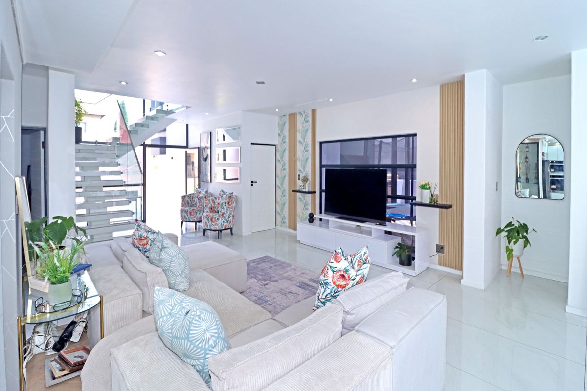 Modern open-plan living area featuring a striking floating staircase with glass balustrade, sleek tiled flooring, and contemporary slatted timber wall accents.