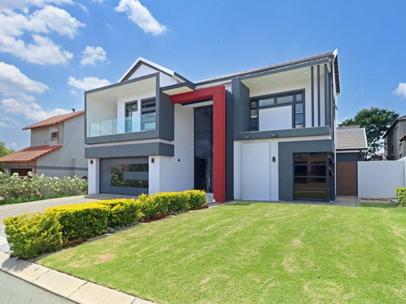 A modern double-story residential property featuring a striking red accent, glass balcony, paved driveway, and well-maintained front garden.