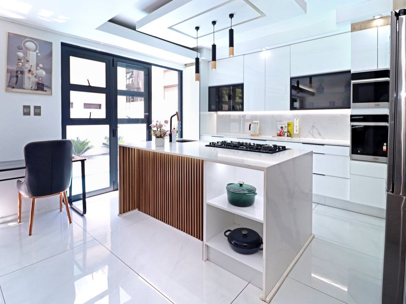 Modern kitchen featuring a central island with slatted wood detailing, stone countertops, integrated gas hob, and high-end built-in appliances with sleek white cabinetry.