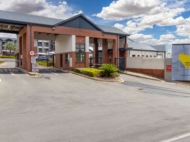 The secure entrance gatehouse of the Canvas Eighty2 apartment complex, featuring brick construction, boom gate access, and professional landscaping.
